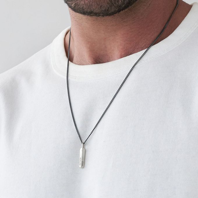 Man wearing a silver vertical bar necklace inscribed with names