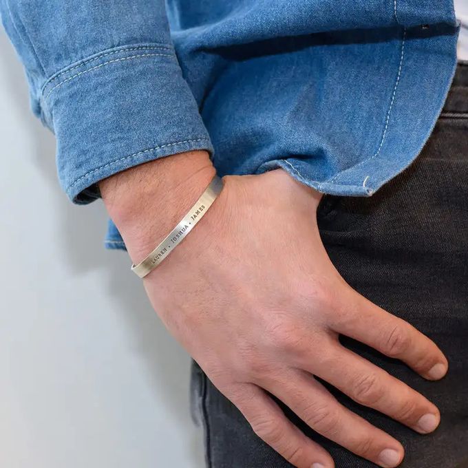 Close-up of a man's hand with a silver inscribed cuff bracelet around his wrist