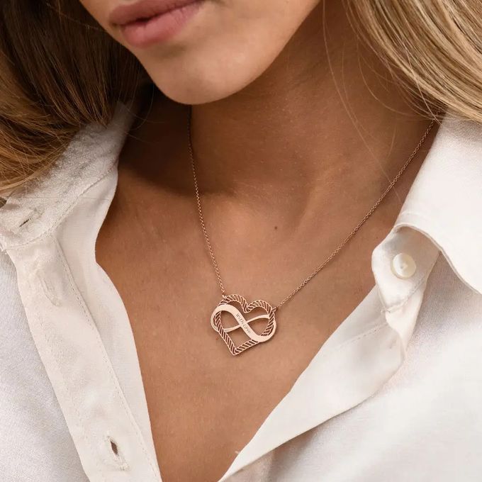 A rose gold necklace with a design that combines heart and infinity sign engraved with names around a woman's neck