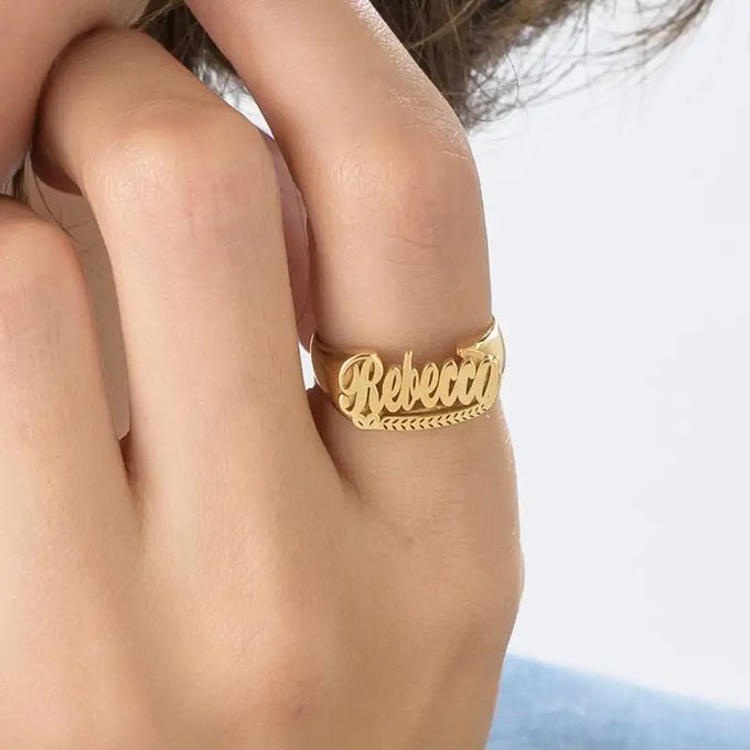 Close-up of a woman's hand with a gold-plated name ring that reads "Rebecca" in a script font on her finger