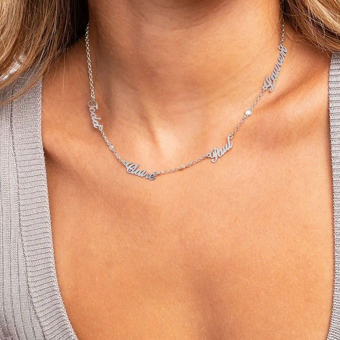 Woman wearing a silver necklace with multiple names dispersed around the chain in cursive font