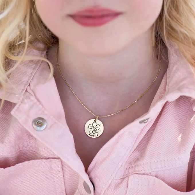 A gold necklace with a circle pendant engraved with a flower drawing and the name "Rebecca"