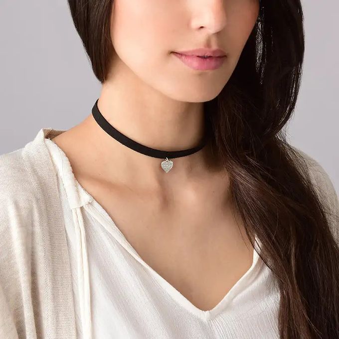 Woman wearing a black choker necklace with heart charm hanging from it