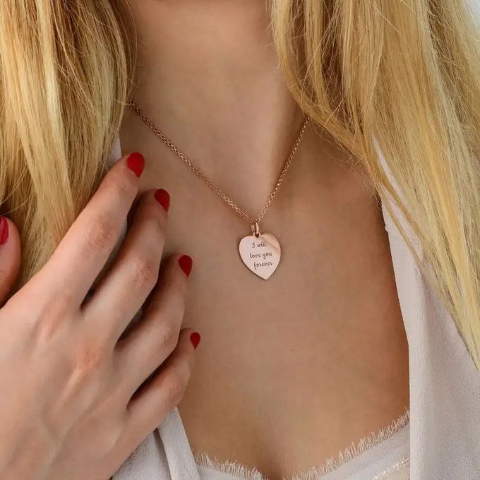A rose gold necklace with a heart-shaped pendant inscribed with "I will love you forever" around a woman's neck