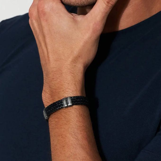 A black braided leather bracelet with silver vertical name tags around a man's wrist
