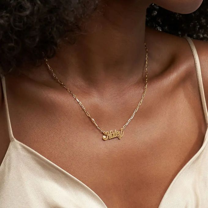 A paperclip gold name necklace that reads "Haley" embellished with a diamond around a woman's neck