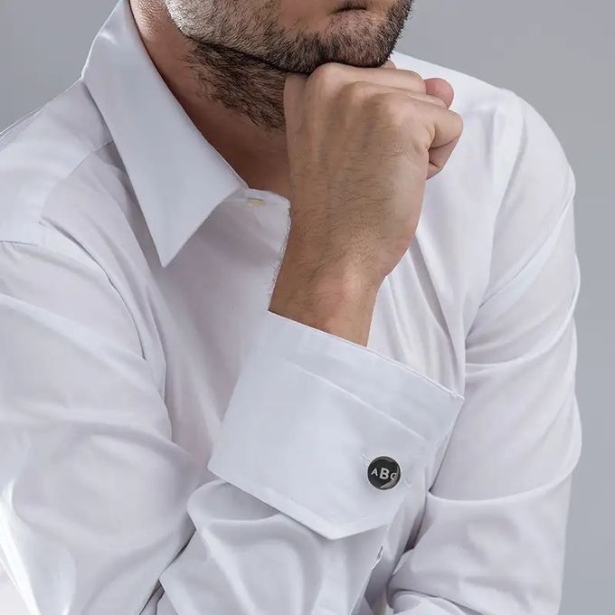 Man in a white shirt with round cufflinks inscribed with "ABC" leaning his chin on his hand
