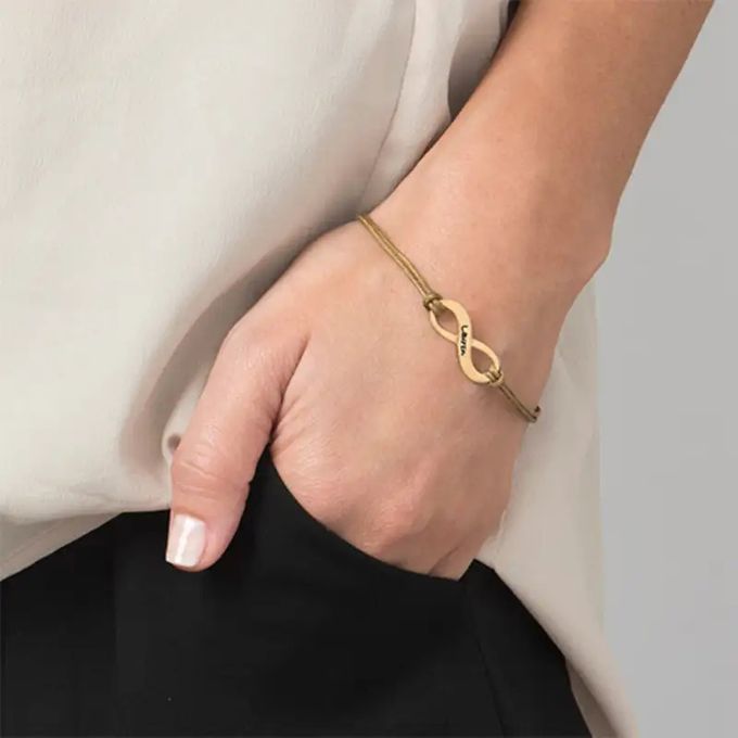 Close-up of a woman's hand in her pocket with a gold infinity-sign bracelet inscribed with a name