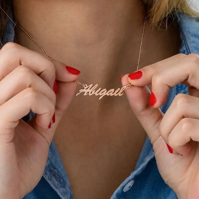 Close up of a woman holding up her name pendant of her rose gold name necklace that reads "Abigail"