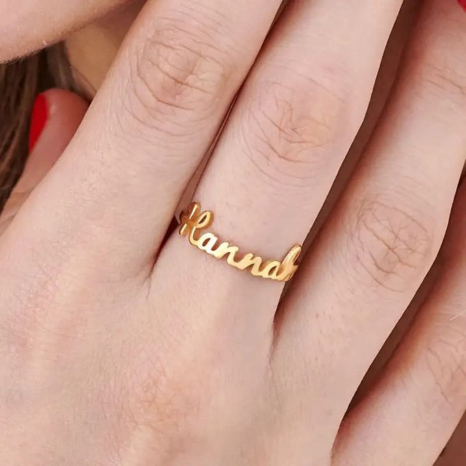 A close up of a gold name ring that reads "Hannah" in a script font on a woman's finger