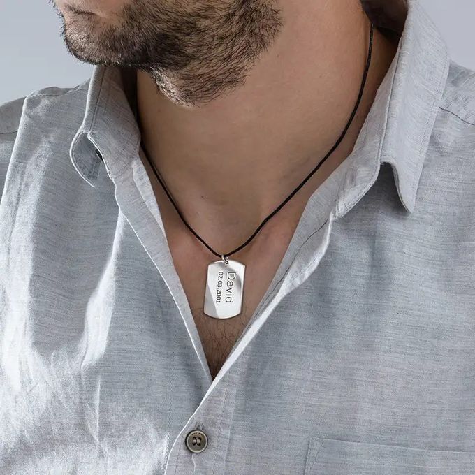 Silver tag necklace with a name and date inscribed around a man's neck