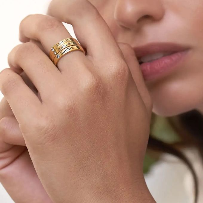 Woman wearing three stackable gold rings with birthstones inscribed with names