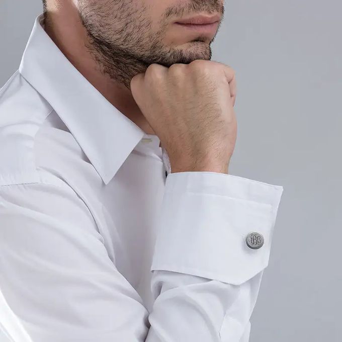 Man in a white shirt with stainless steel monogrammed cufflinks leaning his chin on his hand