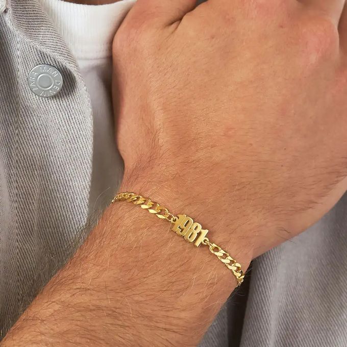 Close-up of a gold thick-chain bracelet inscribed with "1981" around a man's wrist