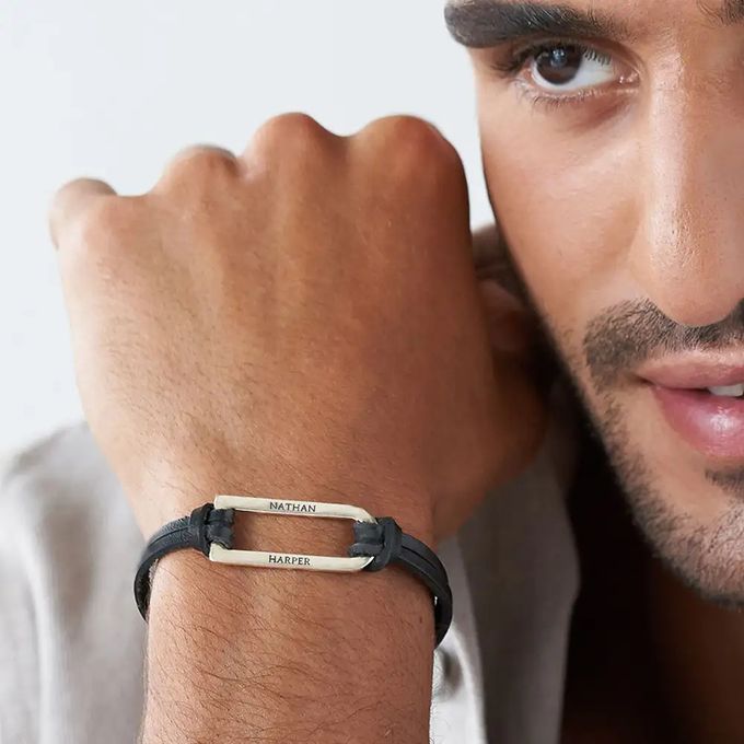 Man wearing a black leather bracelet with a silver inscribed bar