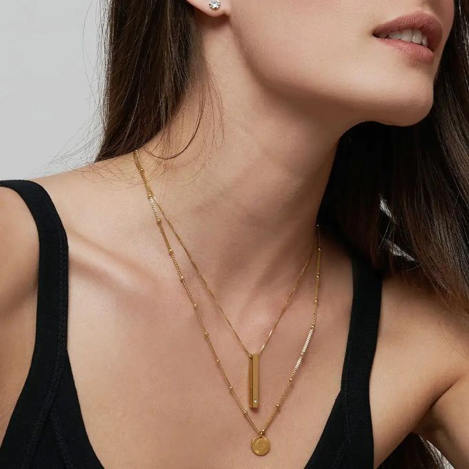 Woman wearing two gold necklaces with bar and round pendants
