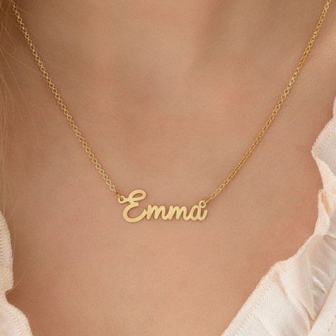 Emma Tiny Cursive Name Necklace in 18K Gold Plating a woman wearing a gold necklace with the word Emma on it