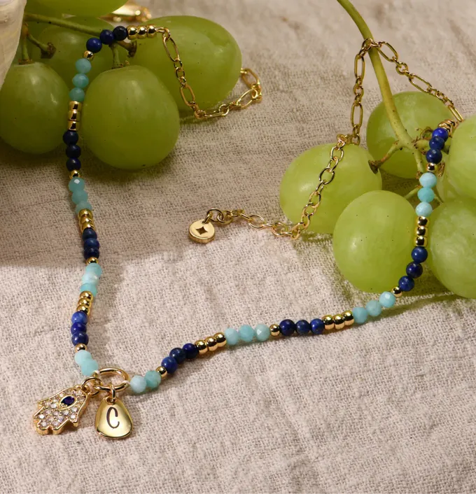 a close up of grapes and a hamsa necklace with blue and gold chain