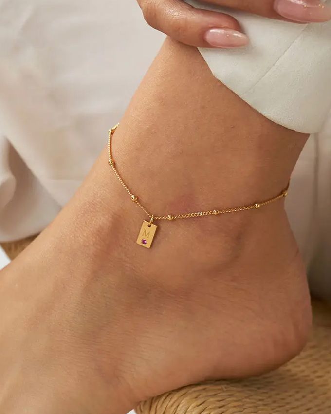 Initial Birthstone Tag Anklet a woman's foot with a gold ankle chain