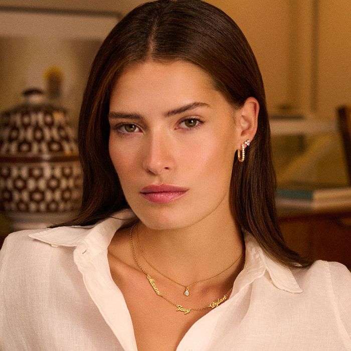 a woman in a white shirt wearing a gold necklace with multiple names