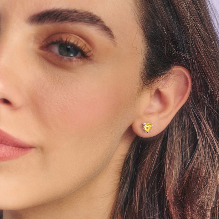 a close up of a lady wearing a pair of earrings with a yellow birthstone