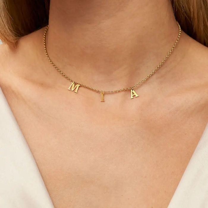 A gold choker with letters spelling out MIA hanging from it around a woman's neck