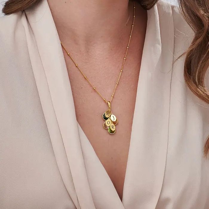 A gold necklace with multiple colorful birthstone pendants and round gold pendants inscribed with initials around a woman's neck