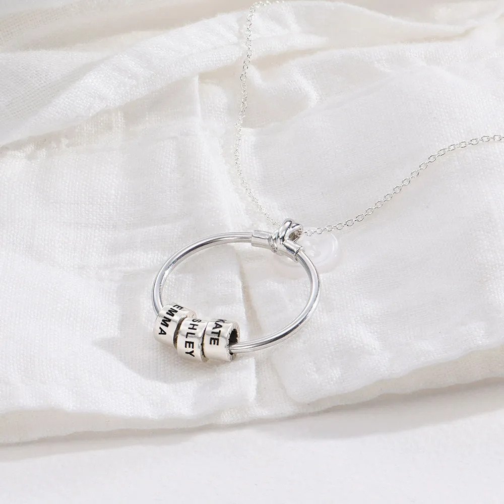 Sterling silver necklace with a circle pendant with inscribed beads laid on a white material