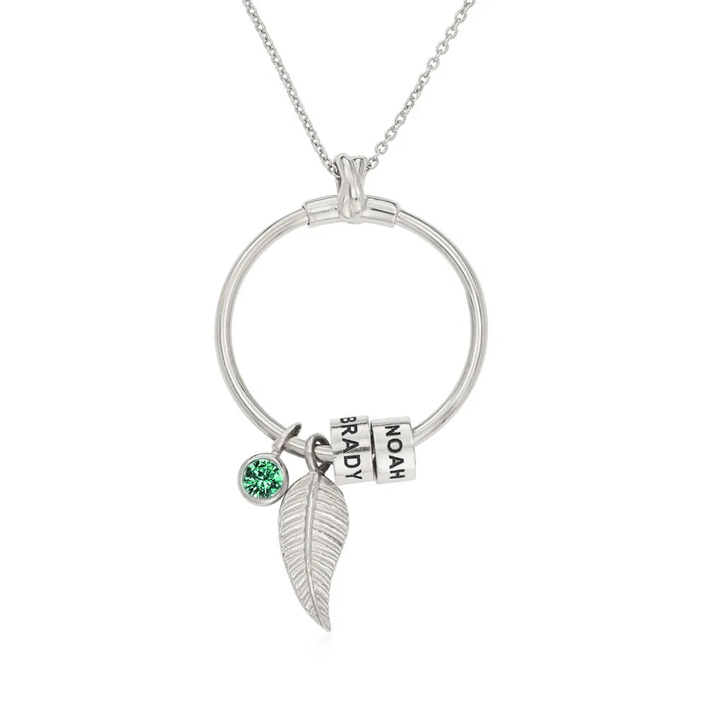 Stock image of a silver necklace with a circle pendant with inscribed beads and a green crystal