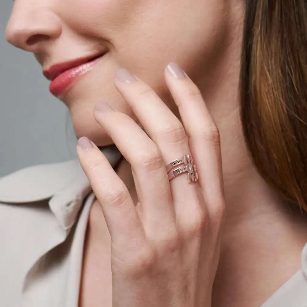 Woman wearing a rose gold ring shaped to spell out "Mom" with a diamond