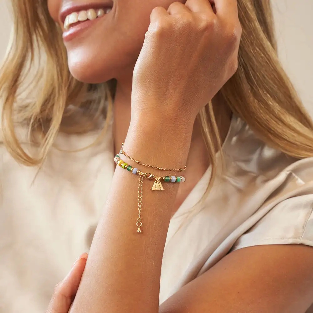 Woman smiling and wearing a layered bracelet with colorful beads and a gold chain with gold charms