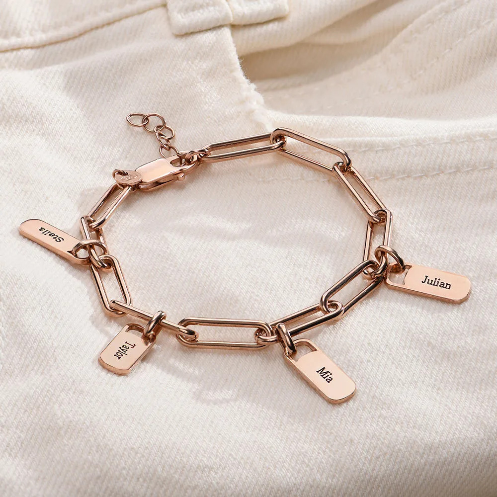 Rose gold charm bracelet with names inscribed on the charms displayed on white jeans