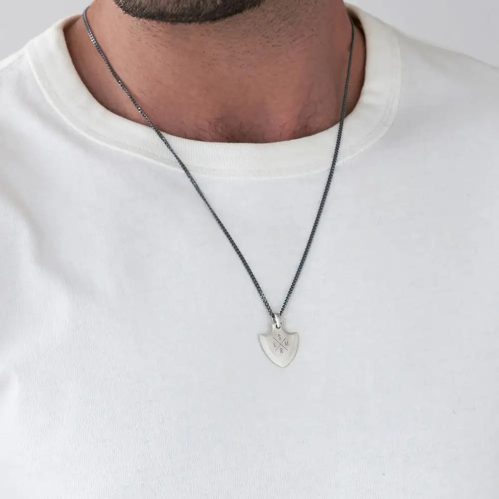 A silver necklace with a shield-shaped inscribed pendant around a man's neck