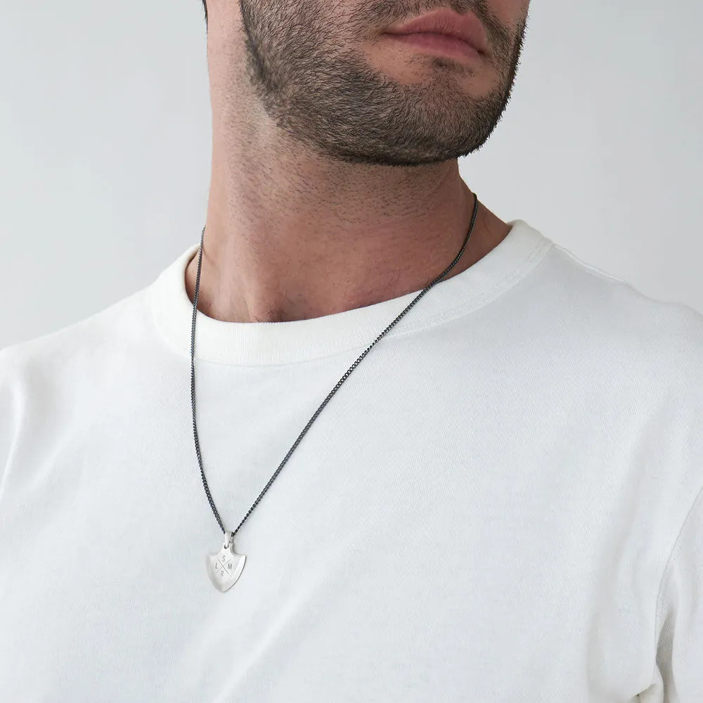 Man wearing a silver shield-shaped engraved necklace around his neck