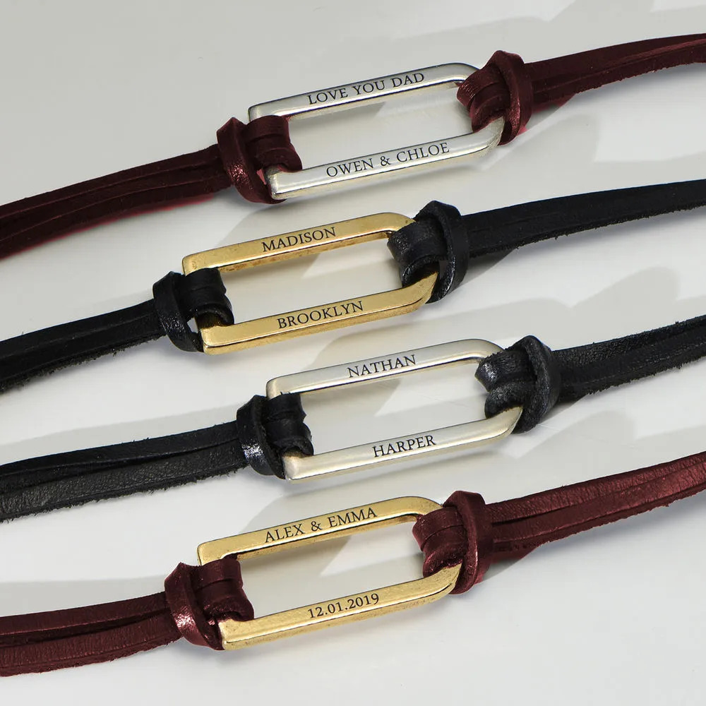 Stock image of black and brown leather bracelets with gold and silver inscribed bars 