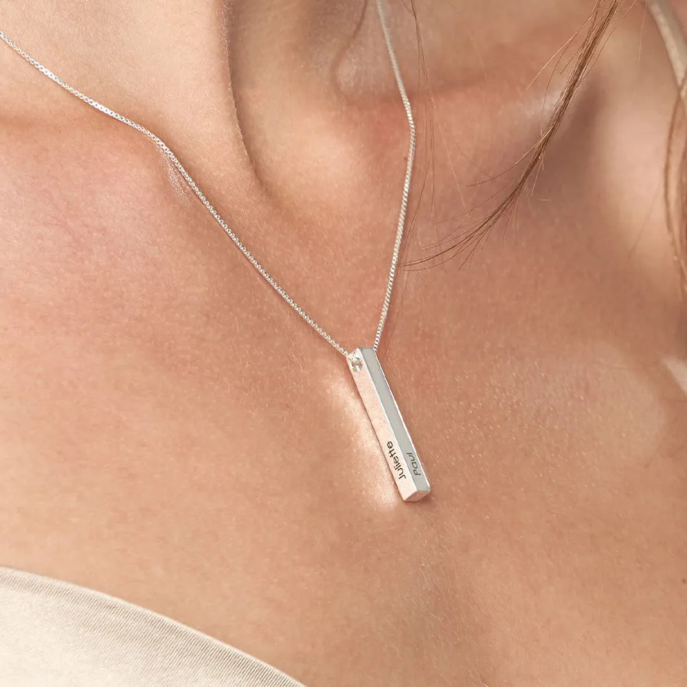 Close-up of a silver necklace with an inscribed vertical bar pendant around a woman's neckl