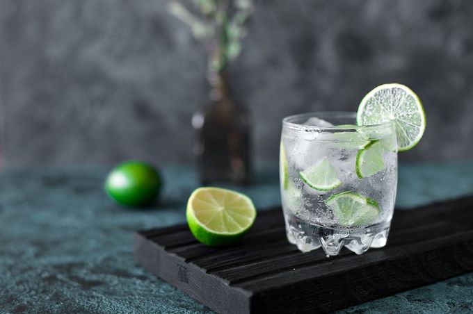 a glass of vodka tonic with ice and lime slices