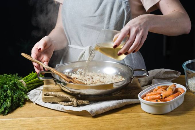 a woman adding white wine to the rice with shrimp