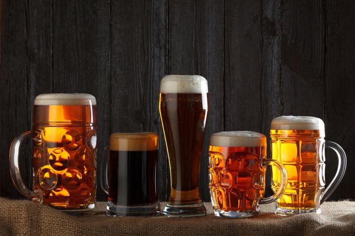 Glasses and glass mugs of Ales and lagers standing in a row with black wooden wall on the background
