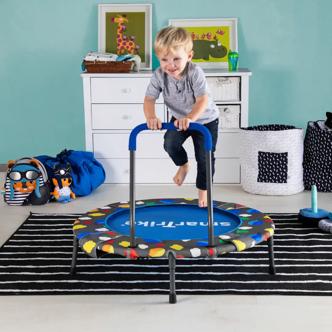 A little boy jumping on a trampoline in a room