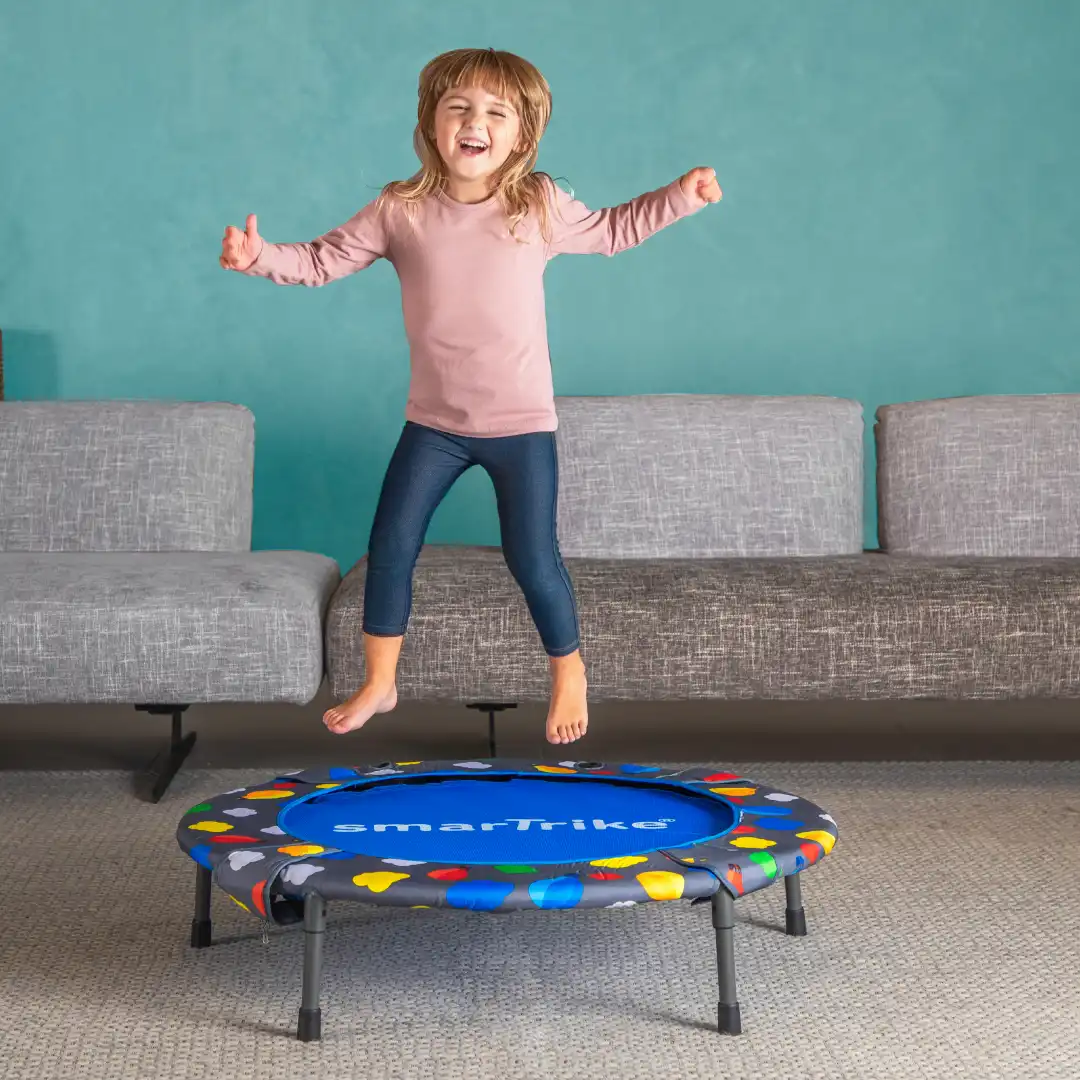 A little girl jumping on a trampoline in a living room