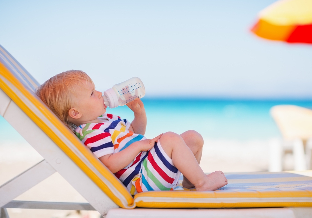 A child on a beach drinking water to stay hydrated and prevent overheating