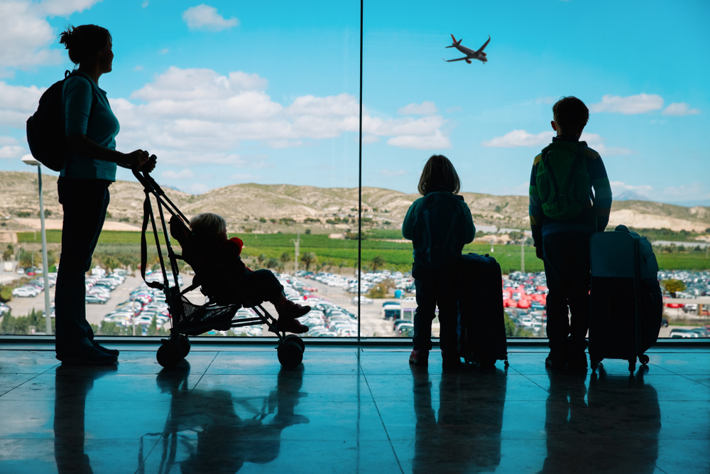 A mother with a baby in a stroller and two older kids with luggage at an airport