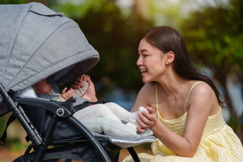 A baby comfortably seated in a shaded stroller with their mom next to it 