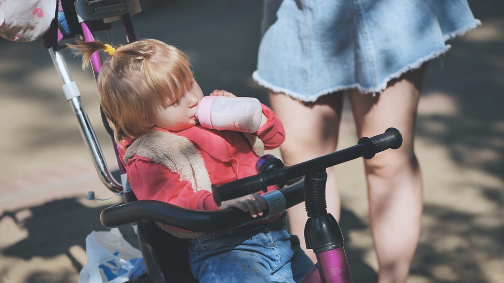 Baby drinking from a botte while sitting on a stroller trike