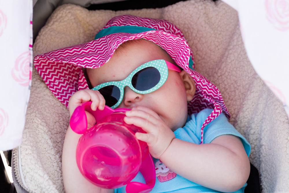 A baby being kept cool in a shaded stroller and sucking on their water bottle