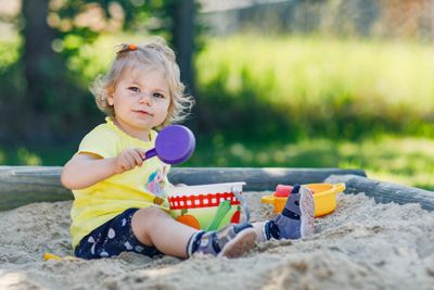 A baby girl enjoying a fun outdoor summer activity - playing in a sandbox 