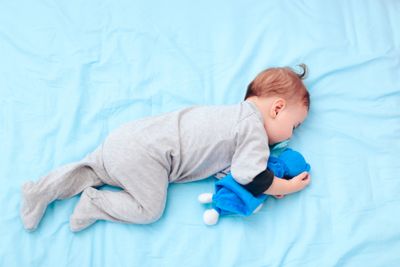A baby in a cotton onesie sleeping next to a stuffed animal, safe from heat rash