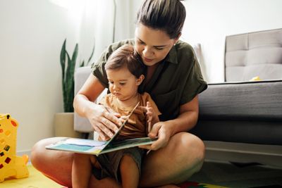 Mother assisting her child's development by reading to them from a book