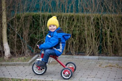 A toddler riding a trike in a blue jacket and a yellow hat